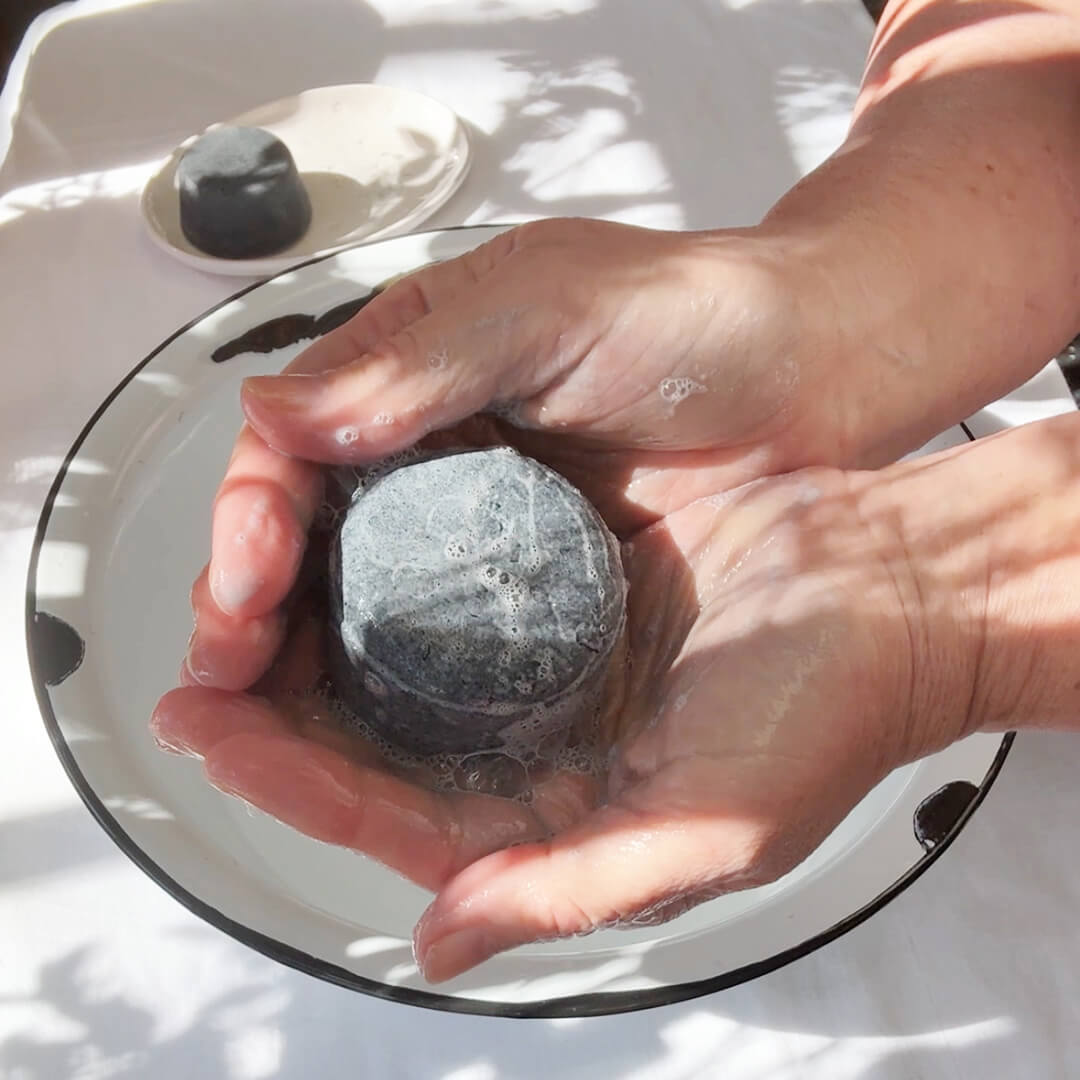Person lathering JDBotanics oily hair shampoo bar in hands showing rich botanical lather